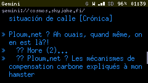 Cosmos on the Cardputer at 2x, deep into the page: a line ending situación de calle [Crónica], then links including Ploum.net ? Ah ouais, quand même, on en est là?! and Ploum.net ? Les mécanismes de compensation carbone expliqués à mon hamster, with a scrollbar on the right about two thirds down